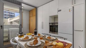 Uma cozinha moderna com armários brancos, forno embutido e geladeira. Há uma mesa de jantar com pratos de comida, incluindo croissants e queijo.