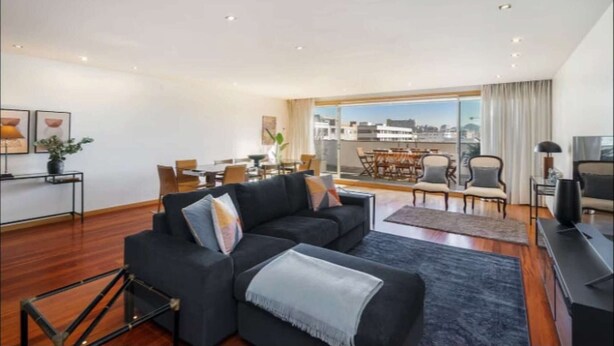 Uma sala de estar moderna com sofá, área de jantar e varanda com vista para a cidade.