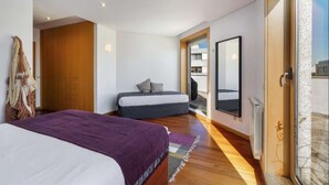 Quarto moderno com uma cama grande, uma mesinha de cabeceira, um espelho e uma porta de vidro deslizante para uma varanda.