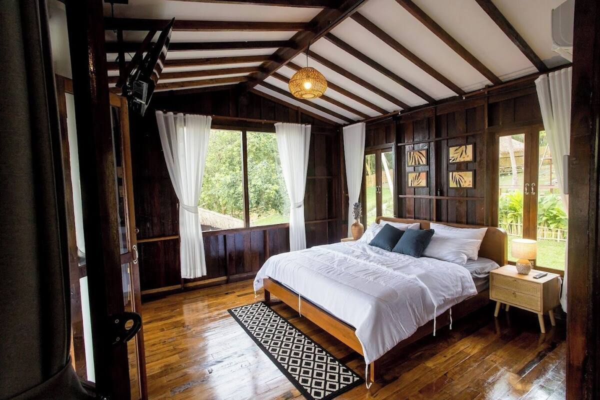 A wooden room with a bed, a nightstand, and a window with curtains.