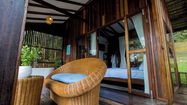Una cabaña de madera con una silla de mimbre y una cama.