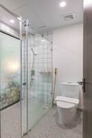 A modern bathroom with a glass shower enclosure, a toilet, and a tiled floor.
