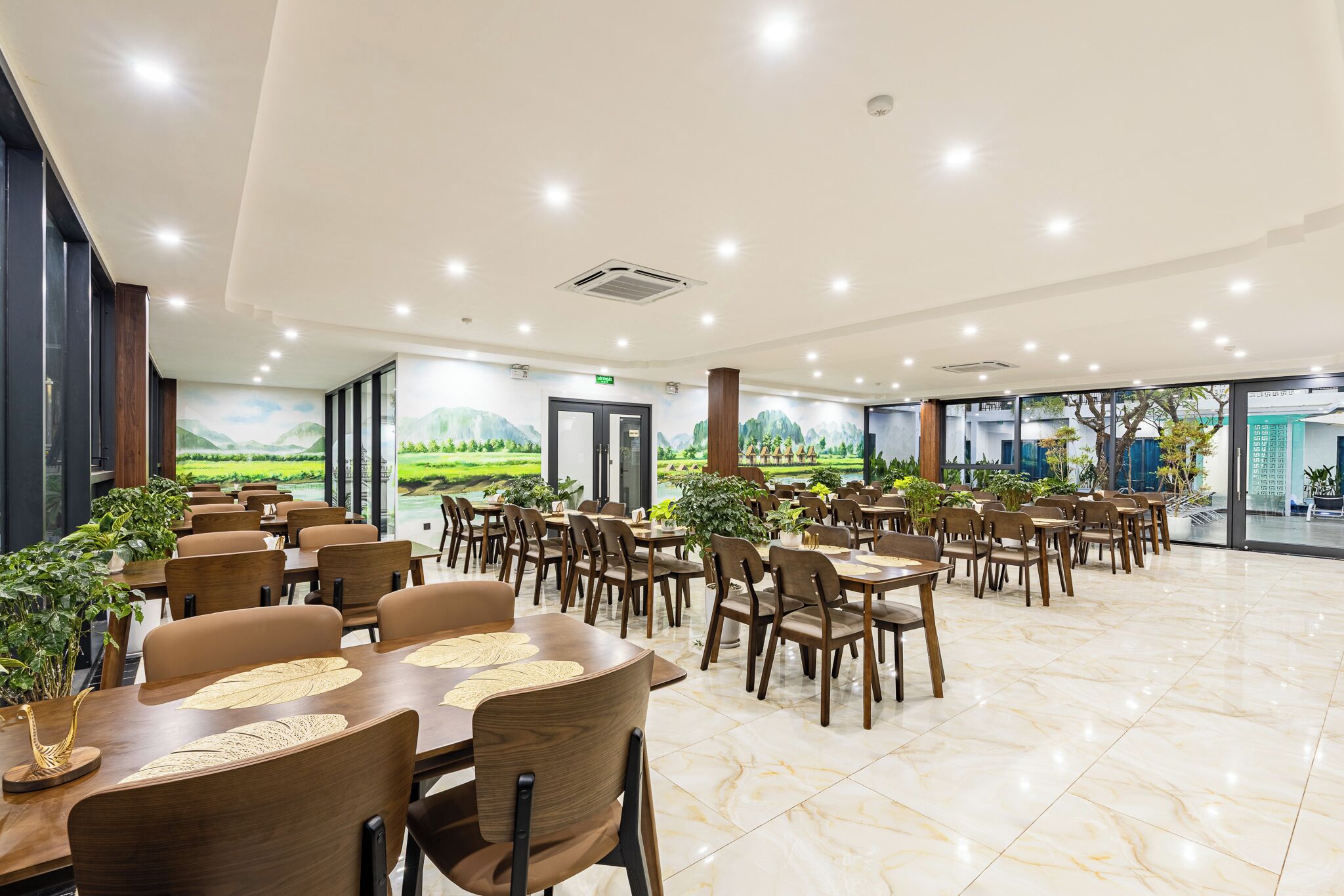 A spacious dining area with multiple tables and chairs, large windows offering a view of a landscaped garden, and a clean, modern interior design.