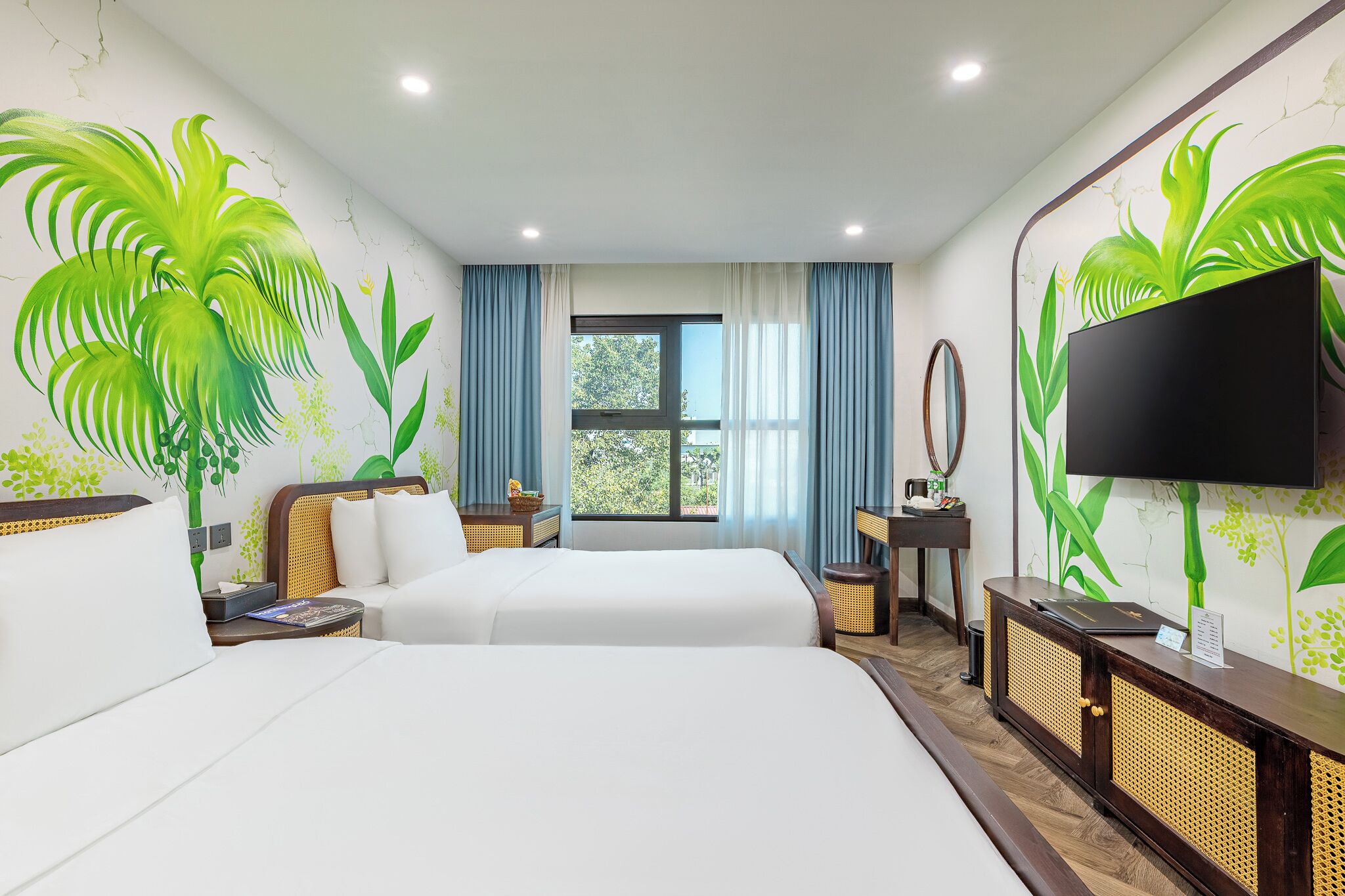 Een hotelkamer met twee bedden, een televisie, een raam met gordijnen en een wanddecoratie van groene bladeren.