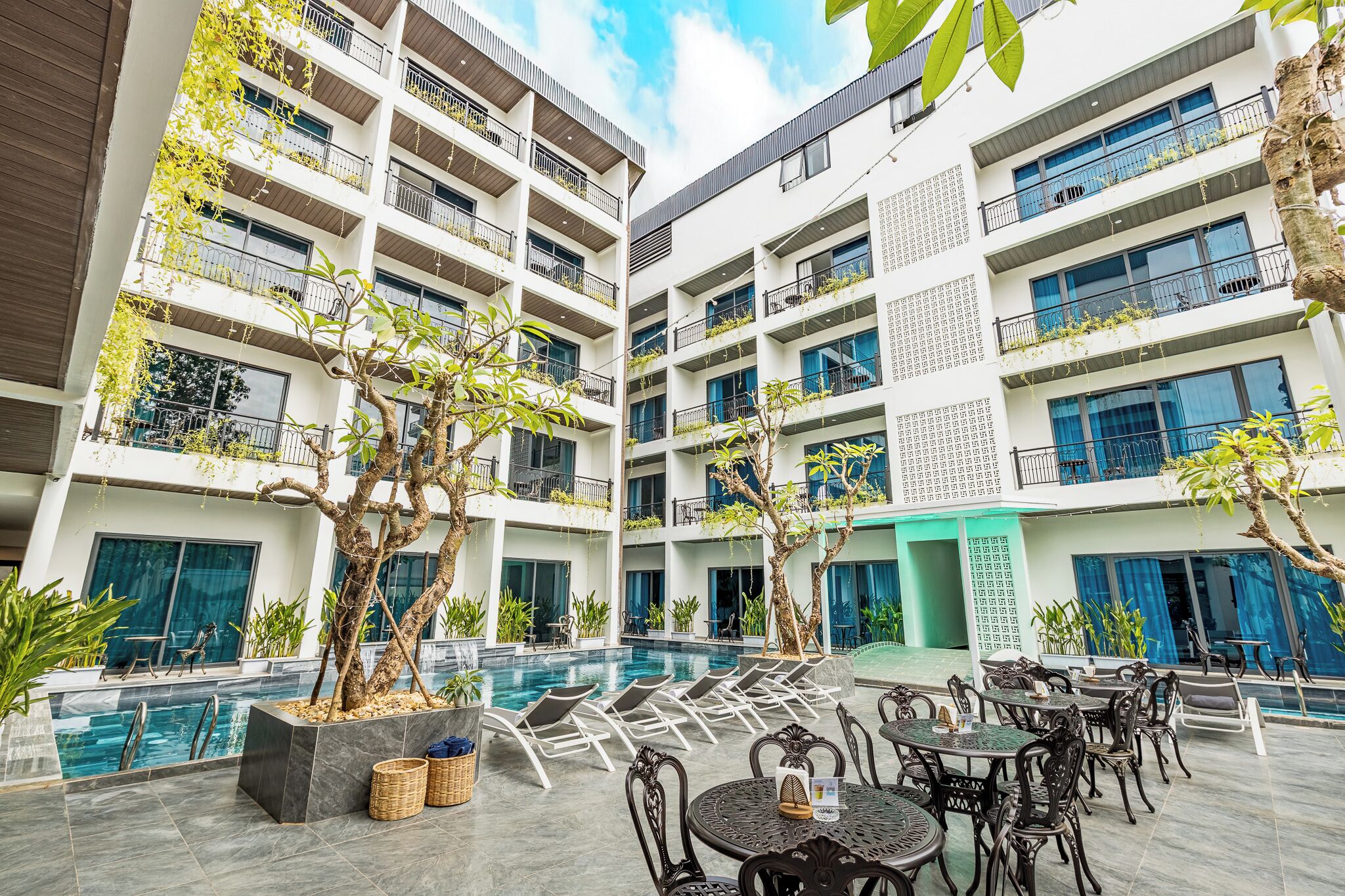 A modern hotel with a central pool, outdoor seating, and multiple balconies with plants.