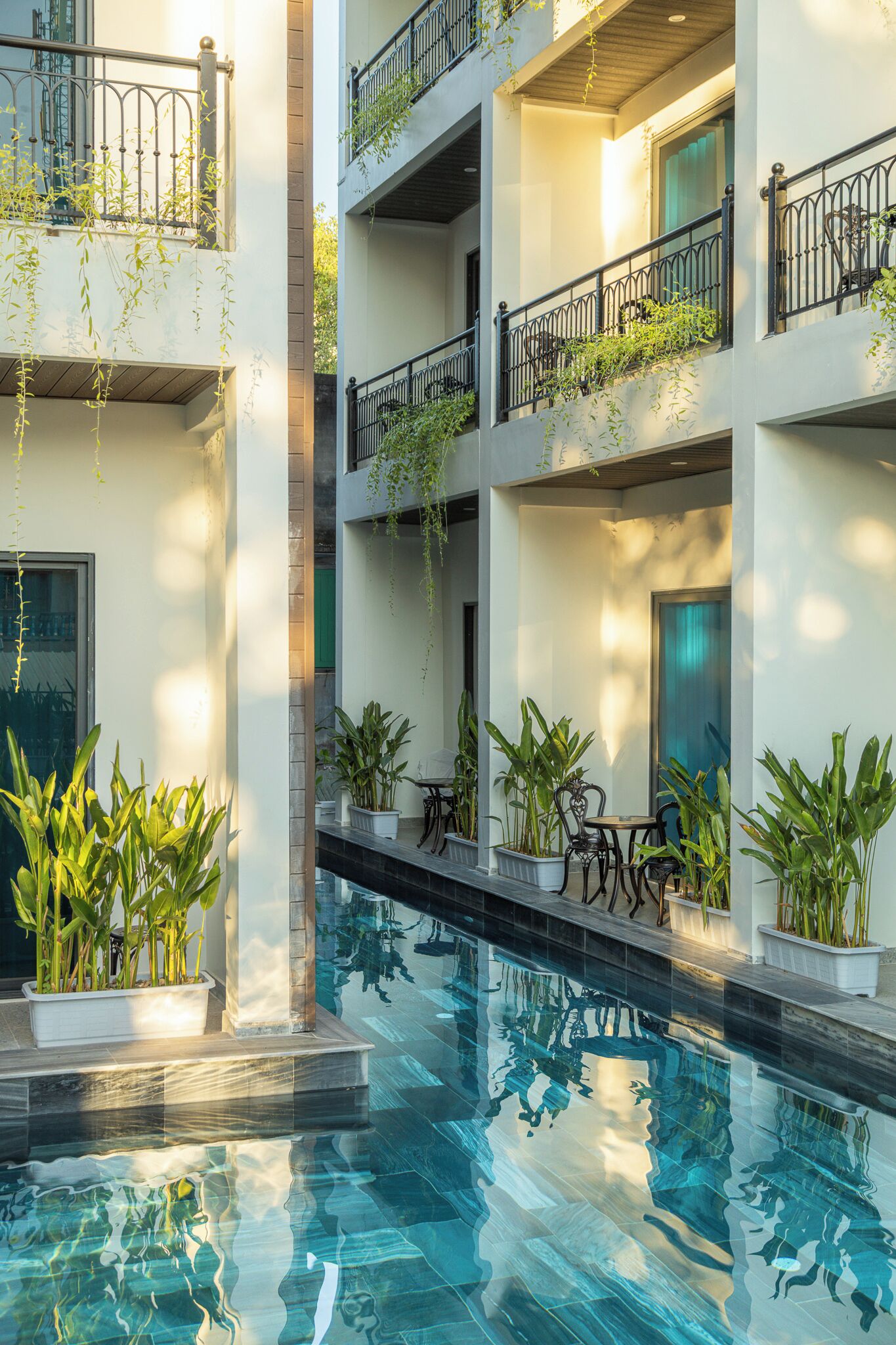 Un edificio de varios niveles con piscina, mobiliario exterior y plantas en macetas.