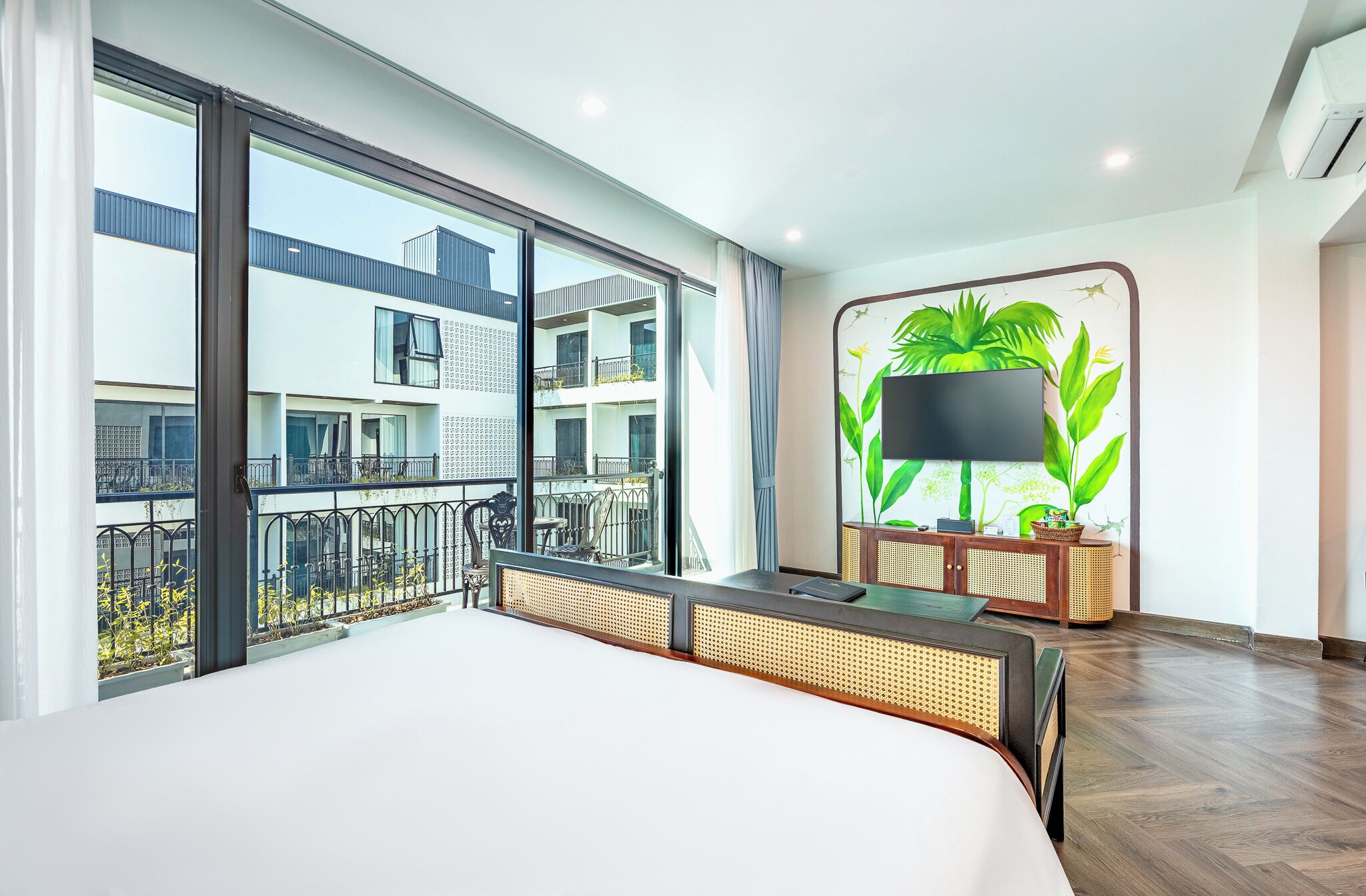 Habitación de hotel moderna con una cama grande, un balcón con vistas a otros edificios, un amplio ventanal y un televisor de pared.