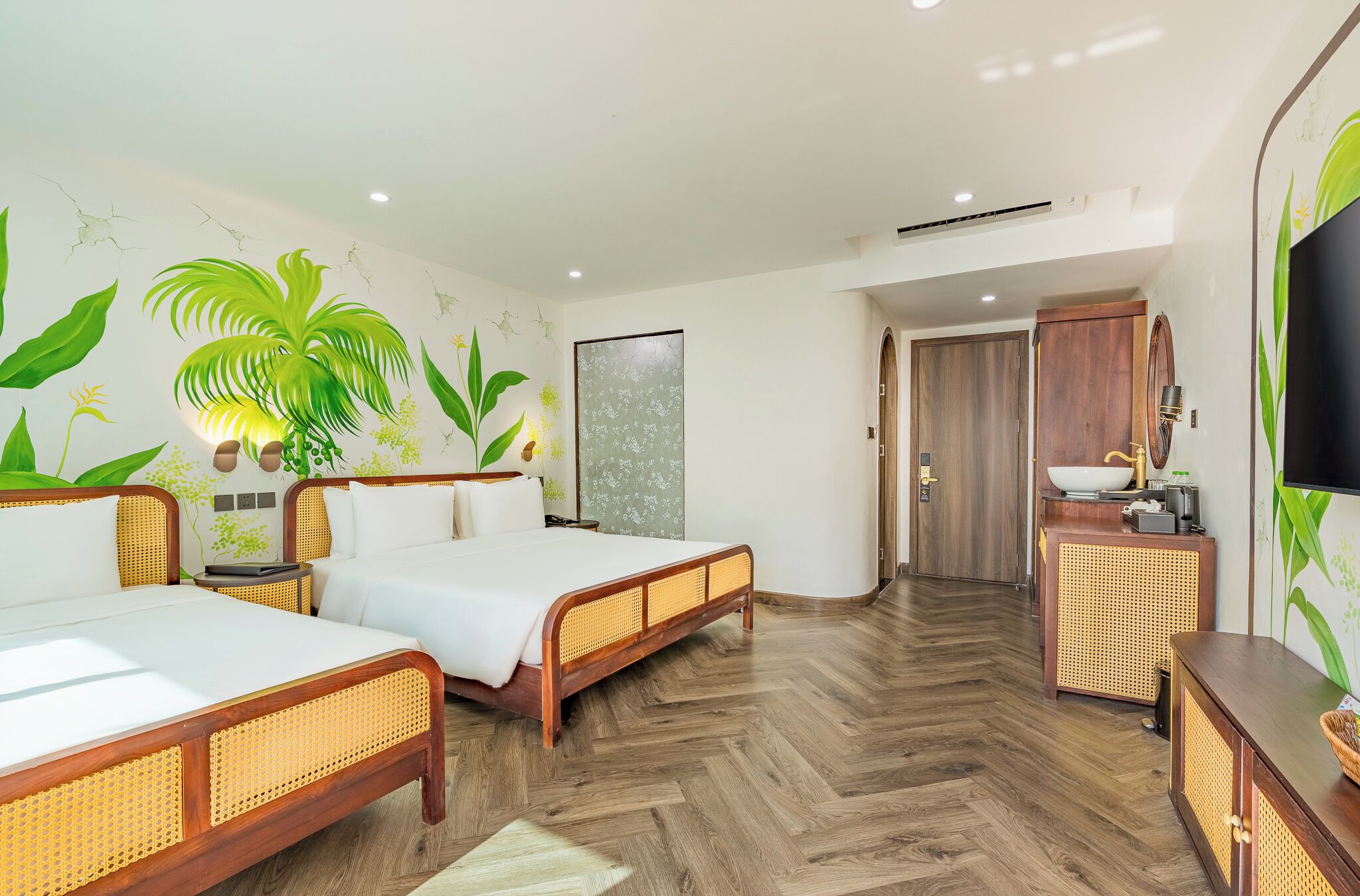 A hotel room with two wooden beds, a large potted plant, a wall-mounted TV, and a wooden cabinet with a sink.