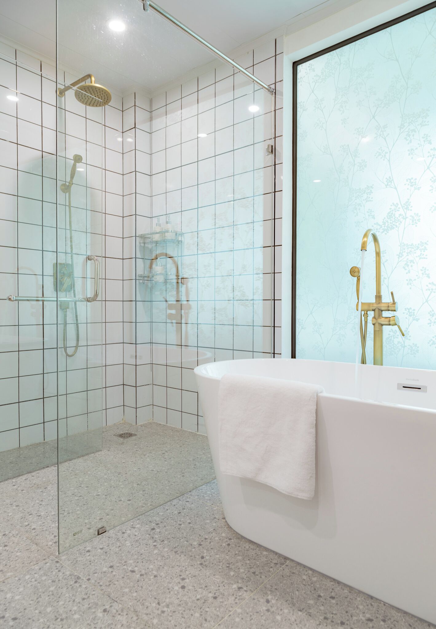 A modern bathroom with a glass-enclosed shower, a freestanding bathtub, and a large mirror with a floral pattern.