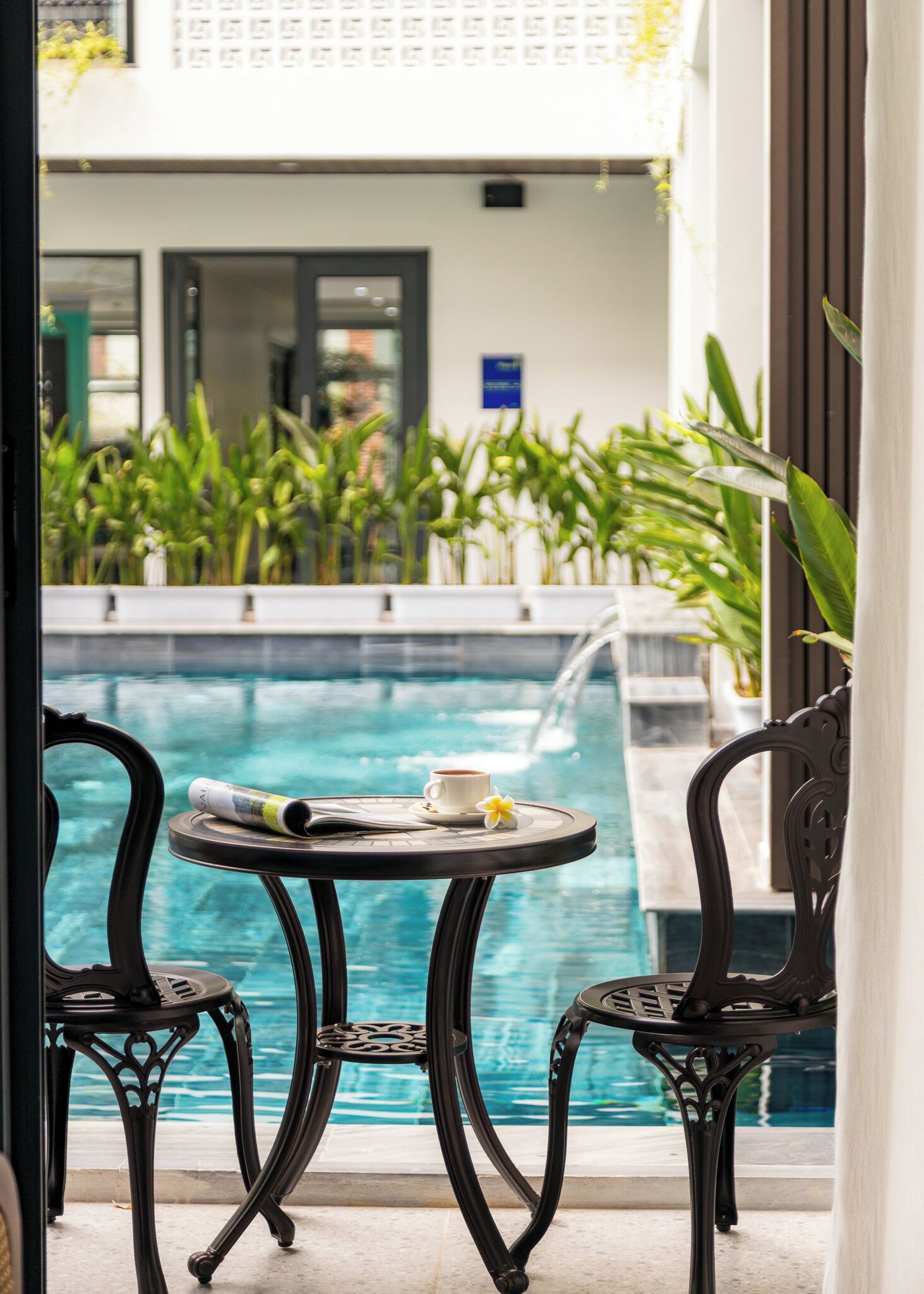 A poolside area with a table and two chairs, a cup of coffee, and a book on the table.