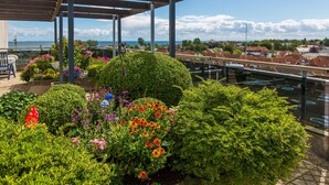 A rooftop garden with a pergola, various plants, and a view of the sea and residential area. - Fantastic view over the Baltic Sea as far as the horizon! (Dahme)