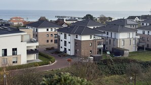 A residential area with modern houses, a visible road, and a body of water in the background. - Fantastic view over the Baltic Sea as far as the horizon! (Dahme)