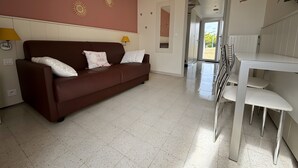 A modern living room with a brown sofa, white cushions, a dining table with chairs, and decorative wall art. - La Perle de l'Océan – Pool and Terrace (Guidel)