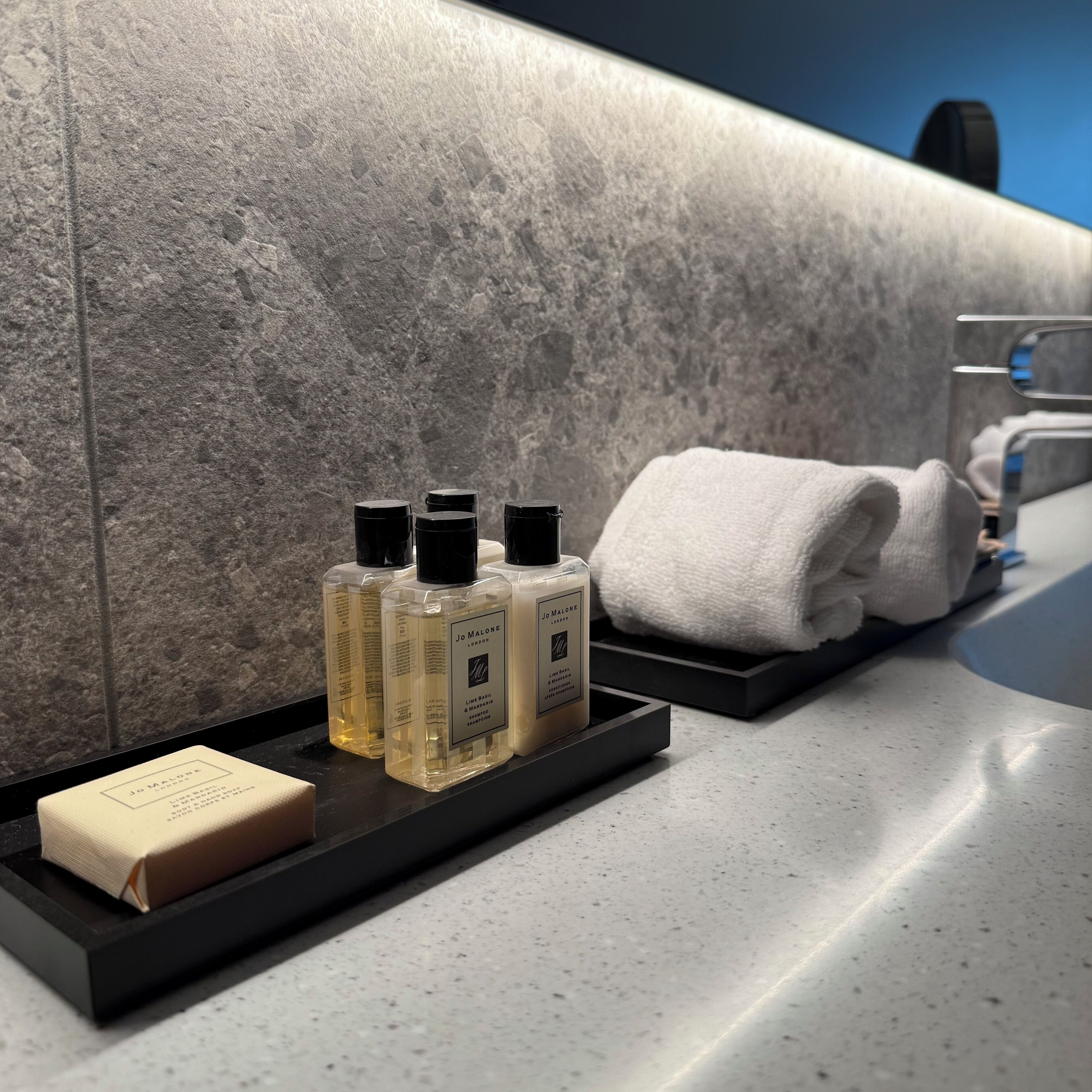 A bathroom with a marble wall, a towel rack, and toiletries including shampoo and soap.