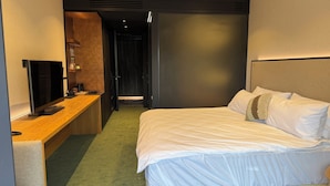 Une chambre d’hôtel comprenant un lit, un bureau avec un téléviseur à écran plat, une machine à café et une porte donnant sur une autre pièce.