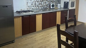 Een kleine keuken met een gasfornuis, magnetron en oven, plus een eethoek met een tafel en stoelen.