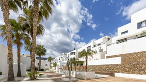 Ein modernes Resort mit weißen Gebäuden, Palmen, einem Poolbereich und einer Steinmauer.