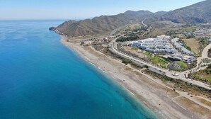 Eine Vogelperspektive auf eine Küstenregion mit einem großen Hotelkomplex, einem Strand und gebirgiger Landschaft.