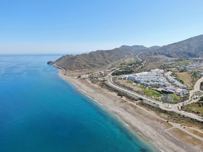 Eine Vogelperspektive auf eine Küstenregion mit einem großen Hotelkomplex, einem Strand und gebirgiger Landschaft.