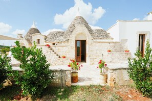 A traditional stone house with a conical roof, a wooden door, and potted red flowers in the entrance area. - Exclusive Luxury Villa MONTE POMPILIO with private infinity pool (Puglia)