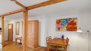 Une table à manger en bois, accompagnée de chaises, un buffet en bois et un tableau abstrait aux couleurs vives accroché au mur.