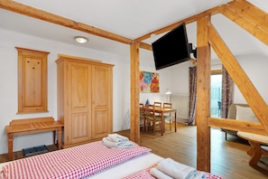 Une chambre à coucher comprenant un lit, une armoire en bois, un bureau, une chaise, une table et un téléviseur fixé à une poutre en bois.