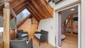 Une terrasse en bois avec des meubles en osier, un plafond incliné et une vue sur l’extérieur.