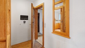 Un couloir avec des portes en bois, un mur blanc et un petit objet noir accroché au mur.