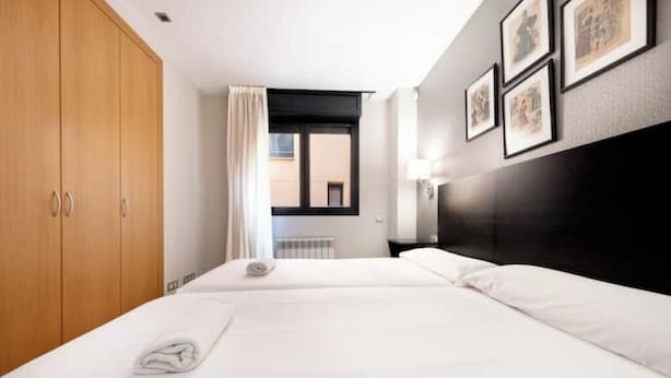 Een hotelkamer met twee bedden, een houten garderobe, een raam met uitzicht en ingelijste foto's aan de muur.