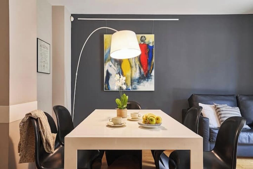 Un comedor moderno con una mesa, sillas, una lámpara, un cuadro y un sofá.
