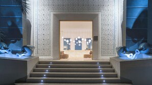 Une entrée imposante agrémentée de motifs décoratifs sur les murs, un espace d’accueil doté d’un bureau moderne et de sièges confortables, et un escalier dont les marches sont illuminées.