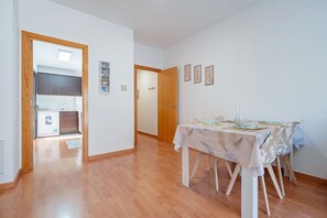 Un comedor con una mesa dispuesta para cuatro personas, una cocina al fondo y un pasillo que lleva a otra habitación.