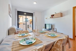 Comedor con una mesa dispuesta para cuatro, un televisor y vistas al exterior.