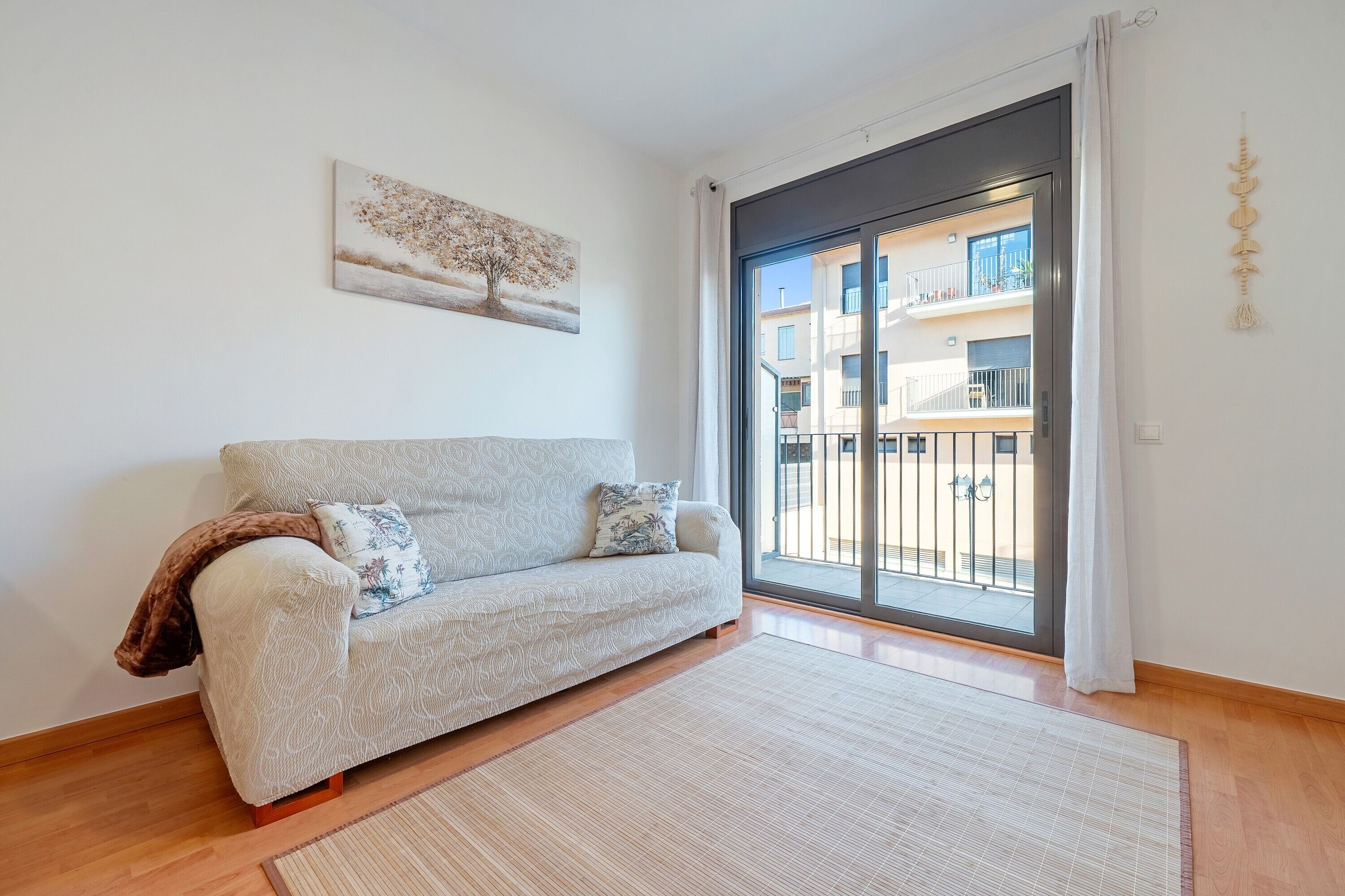 A living room with a sofa, a rug, a painting, and a sliding glass door to an outdoor balcony.