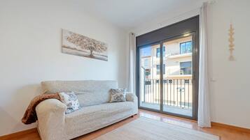 A living room with a sofa, a rug, a painting, and a sliding glass door to an outdoor balcony.