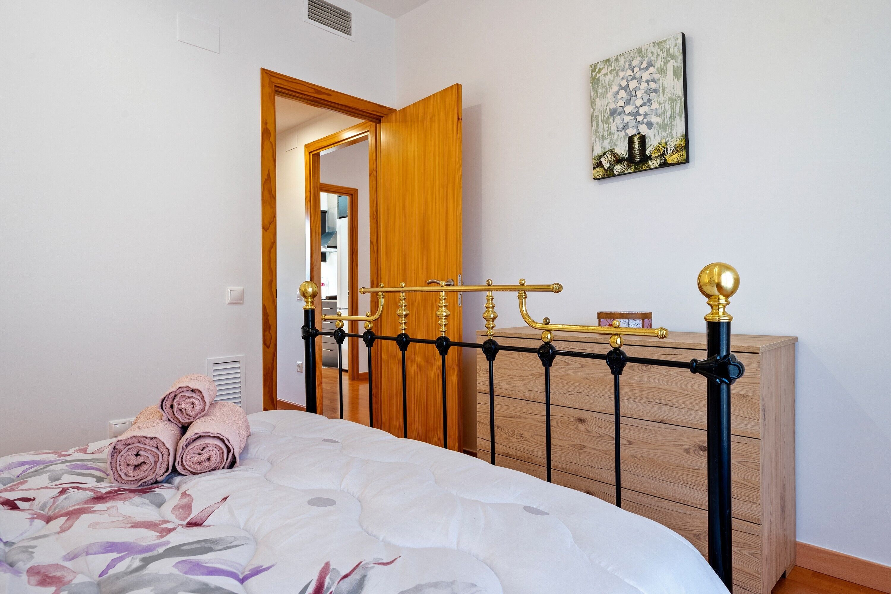 A bedroom with a bed, a wooden dresser, a mirror, and a painting on the wall.