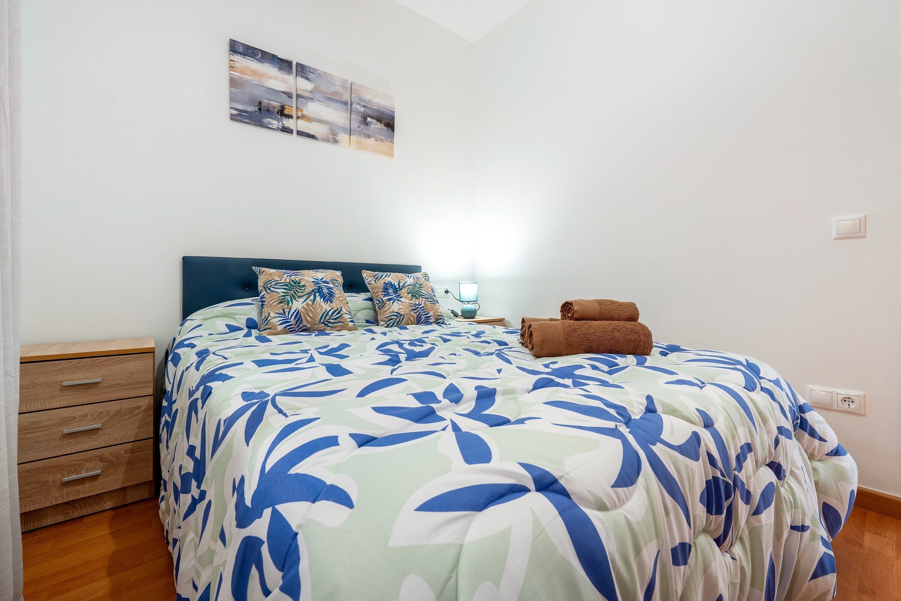 A bedroom with a bed, a nightstand, a lamp, and a wall-mounted artwork.