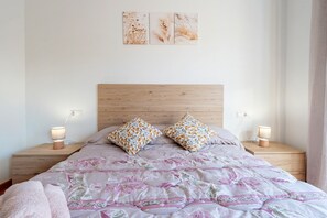 A bedroom with a wooden headboard, a floral bedspread, two bedside lamps, and a nightstand with a lamp.