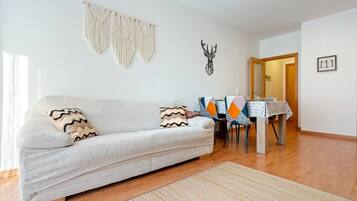 Een woonkamer met een bank, een macramé wanddecoratie, een herten muurstickers en een eethoek met een tafel en stoelen.