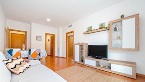 A living room with a sofa, TV, wooden entertainment unit, and a dining area with chairs and a table.