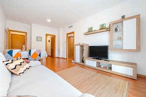 Un salon comprenant un canapé, un téléviseur, un meuble de rangement en bois et un coin repas avec des chaises et une table.