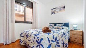 A bedroom with a bed, a nightstand, a window with curtains, and a wall-mounted artwork.