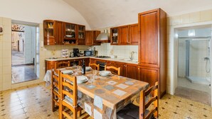 A kitchen with wooden cabinets, a dining table set for four, and a view into the adjacent bathroom. - Apartment 'Gabriele  Salento' with Private Terrace, Wi-Fi and Air Conditioning (Gallipoli)