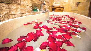 A bathtub filled with rose petals and a stone wall in the background. - Serenity Villa & Spa (Ubud)