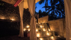 A stone wall with a stone bench and a thatched roof structure. - Serenity Villa & Spa (Ubud)