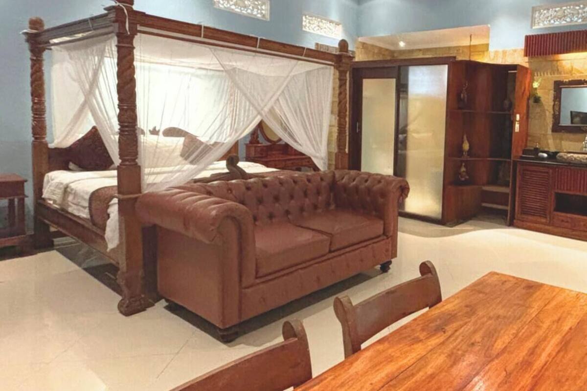 A bedroom with a four-poster bed, a brown leather sofa, and a wooden dining table with chairs.