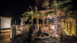 A nighttime outdoor area with a stone fountain, palm trees, and a thatched-roof structure. - Serenity Villa & Spa (Ubud)