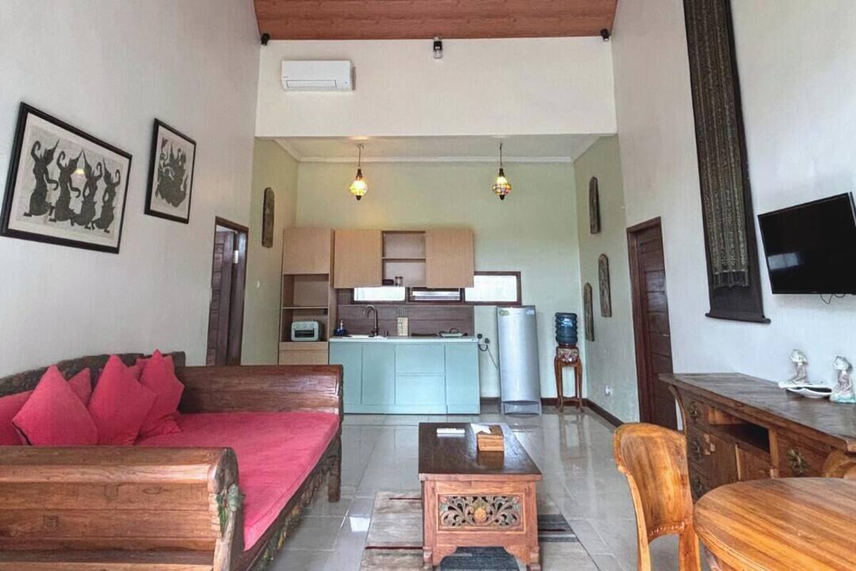 A spacious living area with a wooden sofa, a coffee table, and a wooden dining table. A kitchen is visible in the background with modern appliances.