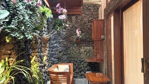 A stone-walled patio with a wooden bench and table, surrounded by potted plants and hanging orchids. - Serenity Villa & Spa (Ubud)