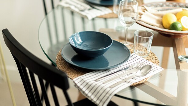 Una mesa de comedor dispuesta con platos azules, un vaso y un plato de limones.